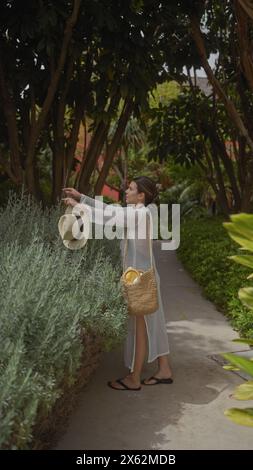 Une jeune femme explore une végétation luxuriante dans un cadre balinais en plein air, tenant décontractée son chapeau de paille et son panier. Banque D'Images