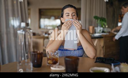 Jeune femme hispanique essuyant la bouche avec serviette au restaurant Banque D'Images