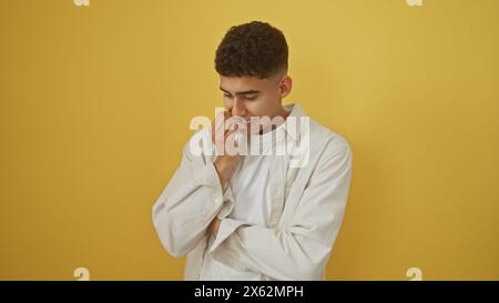 Un jeune homme réfléchi en tenue décontractée se tient sur un fond jaune solide, regardant vers le bas avec une expression pensive. Banque D'Images