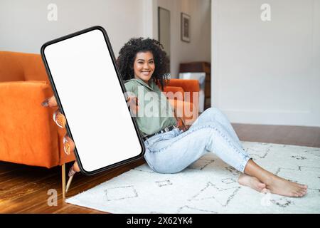 Femme souriante assise sur le sol, tenant un grand smartphone Banque D'Images