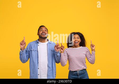 Couple de jeunes excités pointant vers le haut sur un fond jaune vibrant Banque D'Images