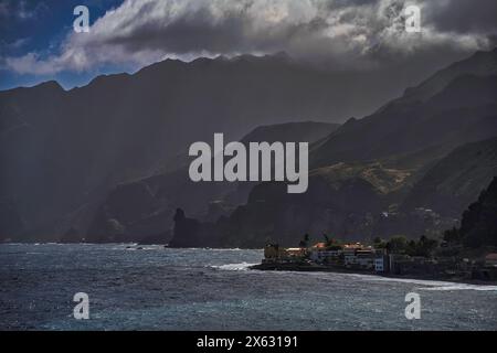 Le village côtier s'accroche au bord des falaises spectaculaires de Santo Antão, tandis que les nuages couvrants projettent des ombres sur le paysage accidenté, créant un c saisissant Banque D'Images
