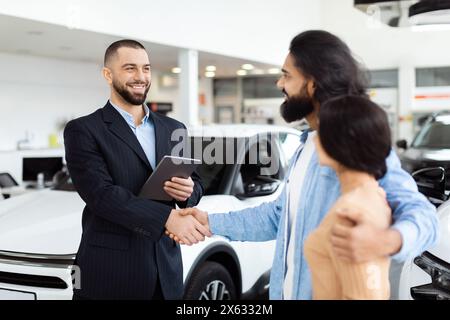 Vendeur professionnel de voitures serrant la main du client dans la salle d'exposition de la concession Banque D'Images