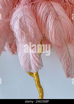 Gros plan de l'abat-jour en plumes d'autruche rose avec support doré contre un mur blanc. Banque D'Images