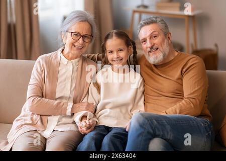 Grands-parents souriants assis sur un canapé avec leur jeune petite-fille Banque D'Images