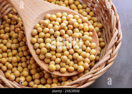 Soja jaune dans un plat en rotin de cuisine avec cuillère en bois. Graines de soja séchées non cuites. Fèves de soja. Bio-produit agricole Banque D'Images