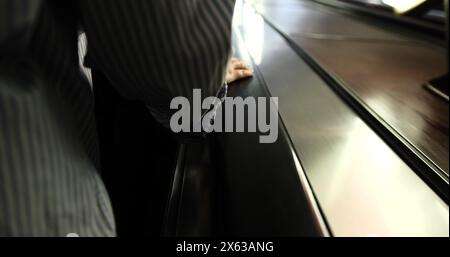 Vue arrière de la main d'une jeune femme noire sur la rampe de l'escalier roulant en mouvement dans le métro de sombre à blanc Banque D'Images