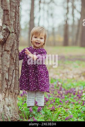 bébé blond dans une robe colorée courant dans une forêt avec des fleurs Banque D'Images