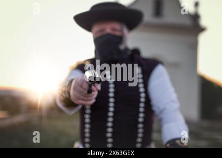 Homme hors-la-loi hongrois betyar en masque noir pointant fusil de chasse au coucher du soleil, mise au point sélective Banque D'Images