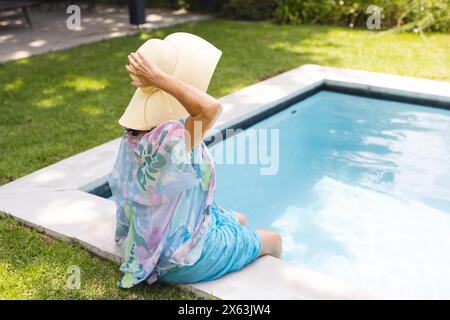 Dehors, femme âgée caucasienne tenant un chapeau près de la piscine Banque D'Images