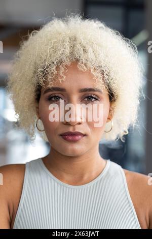 Dans le bureau moderne, jeune femme biraciale avec les cheveux blonds bouclés debout seule Banque D'Images