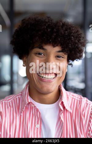 Dans un bureau moderne, jeune collègue masculin biracial portant une chemise rayée, souriant Banque D'Images