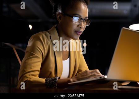 Au bureau, femme d'affaires afro-américaine travaillant tard sur son ordinateur portable Banque D'Images