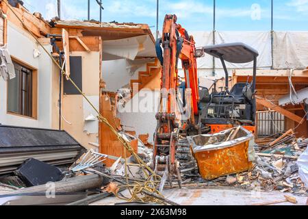Une chargeuse-pelleteuse orange équipée d'un accessoire de pelle hydraulique pour pouvoir saisir les débris lourds lors de la destruction d'un japane traditionnel Banque D'Images