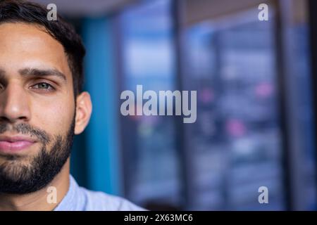 Homme barbu biracial dans une chemise grise décontractée se tient dans le bureau, espace de copie Banque D'Images