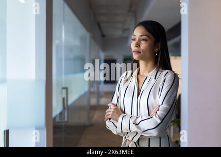 Gestionnaire de sexe féminin biracial d'âge moyen debout au bureau, regardant réfléchi, espace de copie Banque D'Images