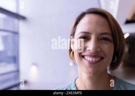 Femme biraciale d'âge moyen souriant à la caméra au bureau, portant des boucles d'oreilles, espace de copie Banque D'Images
