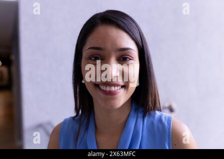 Femme biraciale d'âge moyen portant un haut bleu, souriant chaleureusement au bureau Banque D'Images