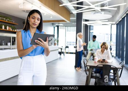 Équipe diversifiée tenant la tablette au bureau, debout devant le fond bleu Banque D'Images