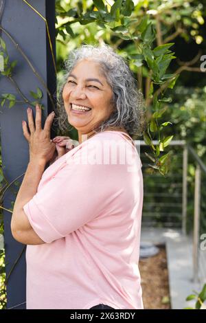 Femme biraciale senior appuyée contre le poteau, souriant dehors Banque D'Images