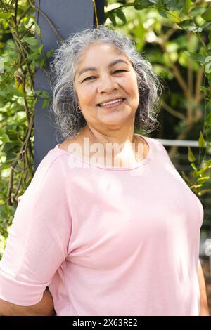 Dehors, femme biraciale senior avec les cheveux gris debout, portant un haut rose, souriant Banque D'Images