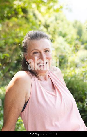 Une femme caucasienne senior portant un haut rose, assise à l'extérieur, souriant à la caméra Banque D'Images