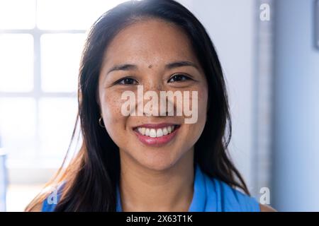 Au bureau, femme d'affaires biraciale en haut bleu, souriant avec confiance Banque D'Images