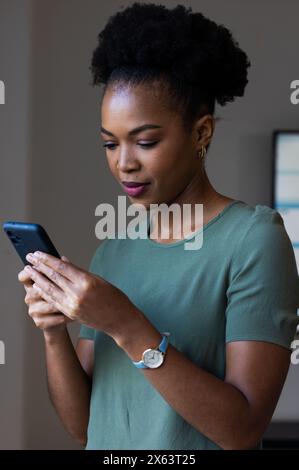 Au bureau, femme d'affaires afro-américaine dans le téléphone vert de vérification supérieure Banque D'Images