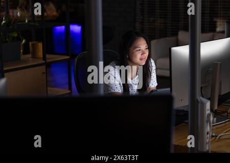 Au bureau, femme d'affaires biraciale étudiant l'écran, travaillant tard Banque D'Images