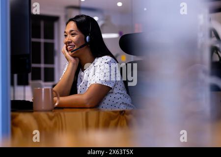 Au bureau, femme d'affaires biraciale portant un casque, travaillant tard Banque D'Images