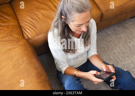 A la maison, femme caucasienne dans une chemise rayée tenant un smartphone Banque D'Images
