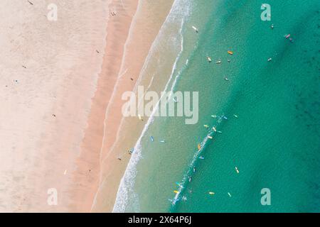 élèves d'une école de surf sur le rivage d'une plage tôt le matin avec peu de monde, vue aérienne de dessus avec un drone. Banque D'Images