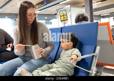 Une femme nourrit un enfant avec une cuillerée de nourriture. L'enfant est assis sur un banc bleu Banque D'Images