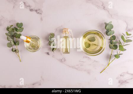 Bol, bouteilles d'huile essentielle d'eucalyptus, bouquet de branches d'eucalyptus fraîches. Ingrédients biologiques naturels pour cosmétiques, soins de la peau. Pose à plat Banque D'Images