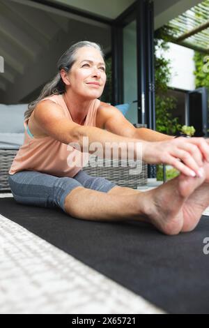 À la maison, femme caucasienne mature s'étirant sur un tapis de yoga Banque D'Images
