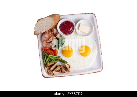 Assiette de petit déjeuner, œufs frits, bacon, champignons rôtis, légumes et garnitures sur fond blanc isolé Banque D'Images
