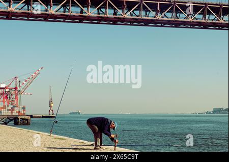 Vieux pêcheur prépare sa canne à pêche sur une monture métallique le long du front de mer du tage. Banque D'Images