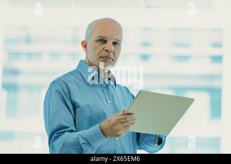 Professionnel chevronné se tient confiant dans un environnement de bureau bien éclairé, tenant une tablette, représentant la détermination Banque D'Images