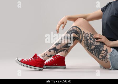 Femme avec des tatouages cool sur fond gris, gros plan Banque D'Images