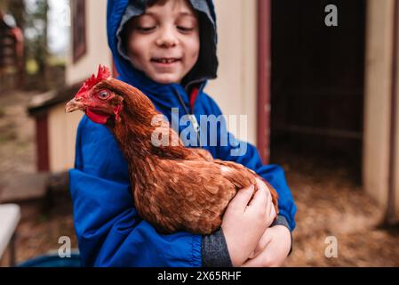 Gros plan du jeune garçon souriant tout en tenant le poulet dehors Banque D'Images