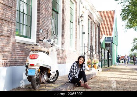 Femme assise sur le trottoir à côté d'un cyclomoteur à Amsterdam Banque D'Images