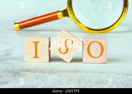 Concept d'ISO. Systèmes de gestion de la qualité. TEXTE iso ÉCRIT sur des cubes en bois avec une loupe en arrière-plan Banque D'Images