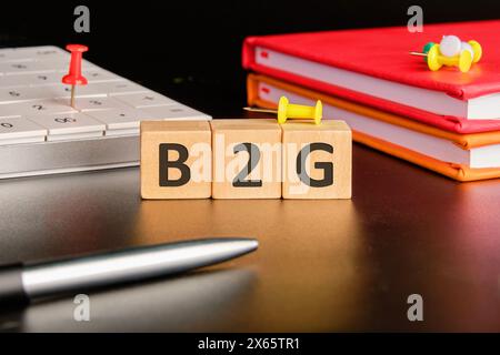 Concept B2G. Affaires au gouvernement. B2G écrit sur des cubes en bois sur fond noir dans une composition avec une calculatrice, des cahiers et un stylo Banque D'Images