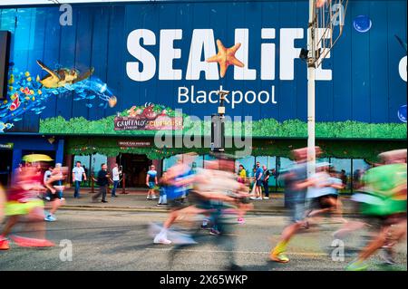 Flou de mouvement des concurrents dans le Blackpool 10K Fun run (2024) le long d'une promenade colorée passant devant le centre Sealife Banque D'Images