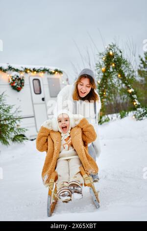 Maman monte sa joyeuse petite fille sur un traîneau en bois en hiver Banque D'Images