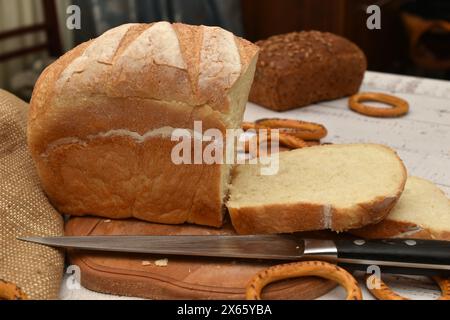 Une miche de pain blanc, cuite à partir de farine de blé, coupée en tranches, repose sur une planche à découper. Banque D'Images
