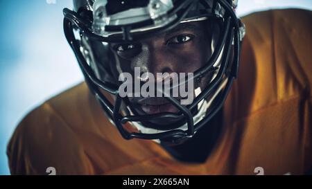 Football américain : gros plan d'un joueur professionnel afro-américain regardant la caméra. Héros athlète prêt à remporter le championnat. Détermination, compétence, puissance. Portrait dramatique Banque D'Images