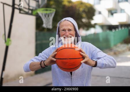 Homme senior jouant au basket-ball à l'extérieur sur le terrain de basket-ball dans la ville. L'homme plus âgé et vital a un mode de vie actif, faisant du sport tous les jours. Banque D'Images