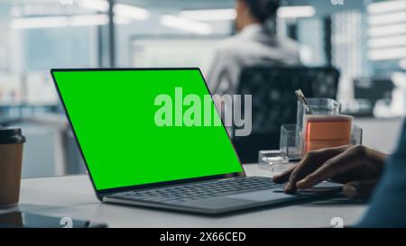 Homme d'affaires noir réussi assis au bureau travaillant sur ordinateur portable à écran vert dans le bureau. Homme d'affaires afro-américain utilisant le pavé tactile sur ordinateur Chroma Key. Prise de vue avec mise au point sur la main Banque D'Images
