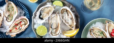 Huîtres sur glace panorama, avec diverses garnitures et verres de vin blanc, plan de pose à plat au-dessus sur un fond de pierre bleue Banque D'Images